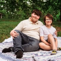 Kieran and Karson sitting together on a picnic blanket outdoors.