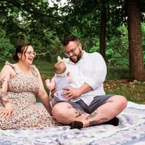 Lauren and Jack sitting outdoors on a picnic blanket with their baby.